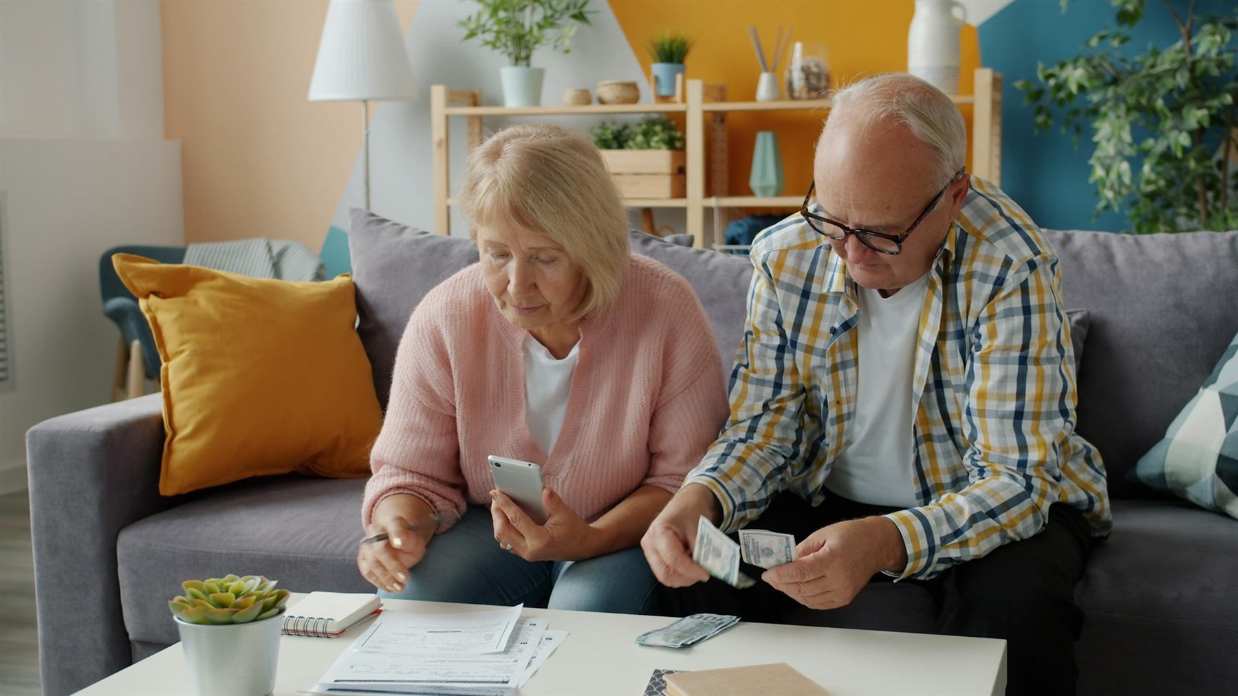 An older couple sitting on a sofa, one holding a phone and the other a bank card