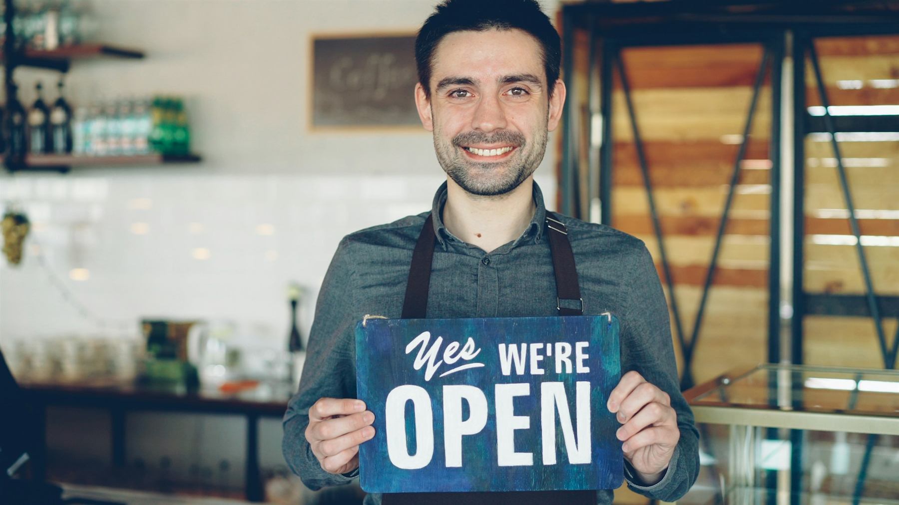 A café owner standing in her doorway holding a sign that says yes, we are open