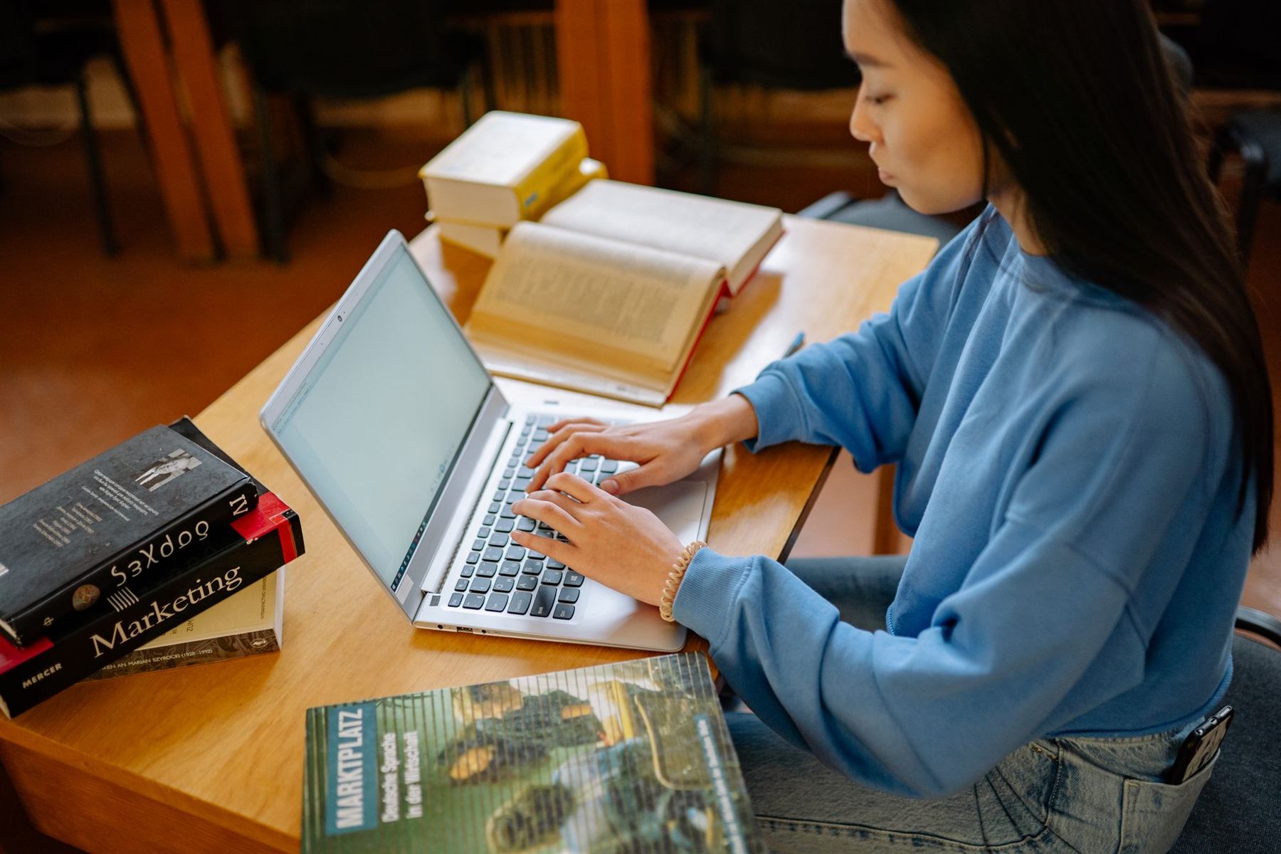 A student working on a laptop surrounded by books