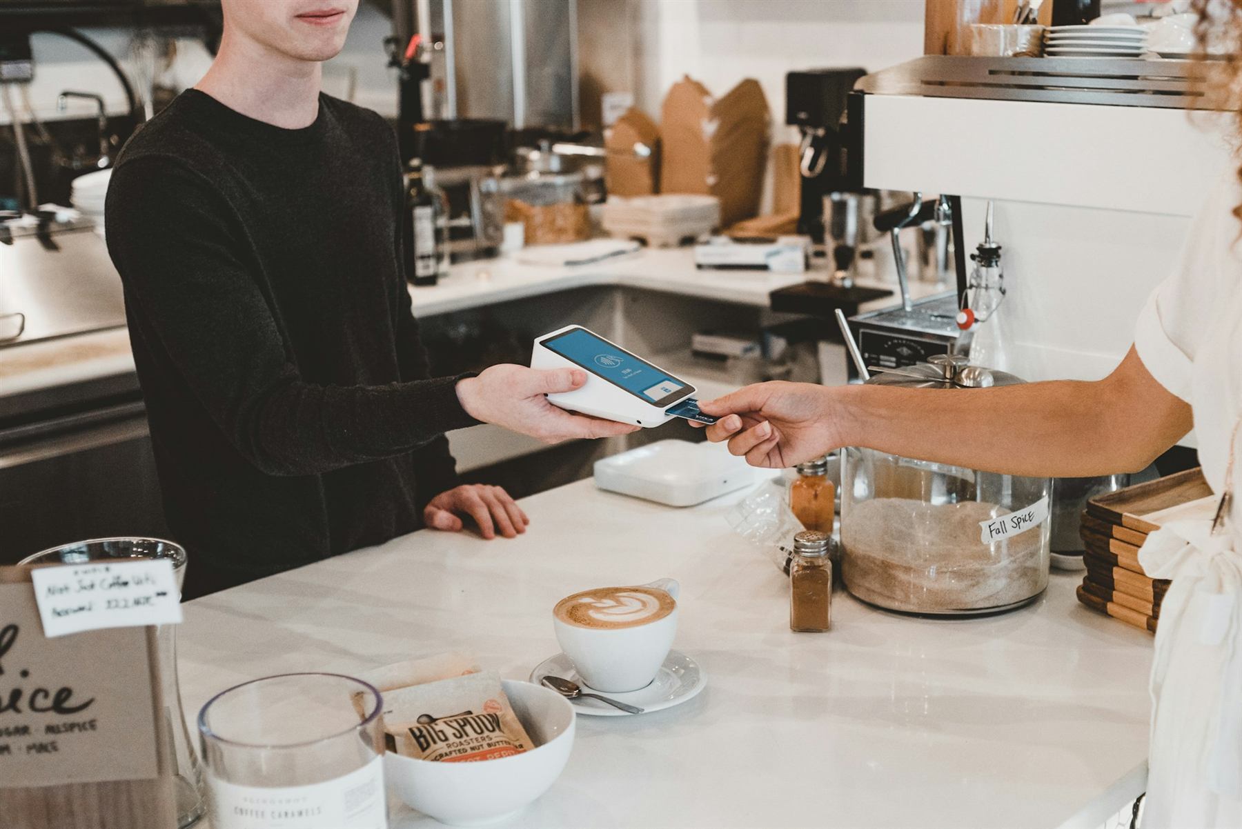 A customer paying by tapping a phone on a card reader at a café counter