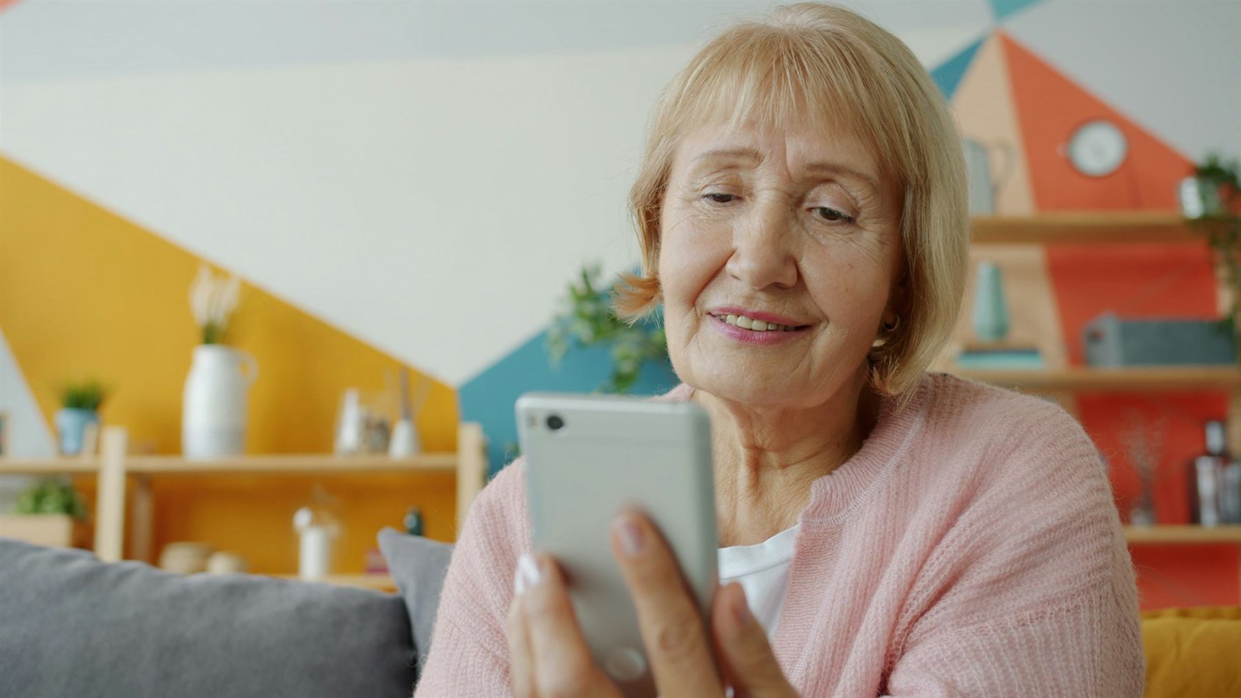 An older woman at home smiling as she reads a message on her phone