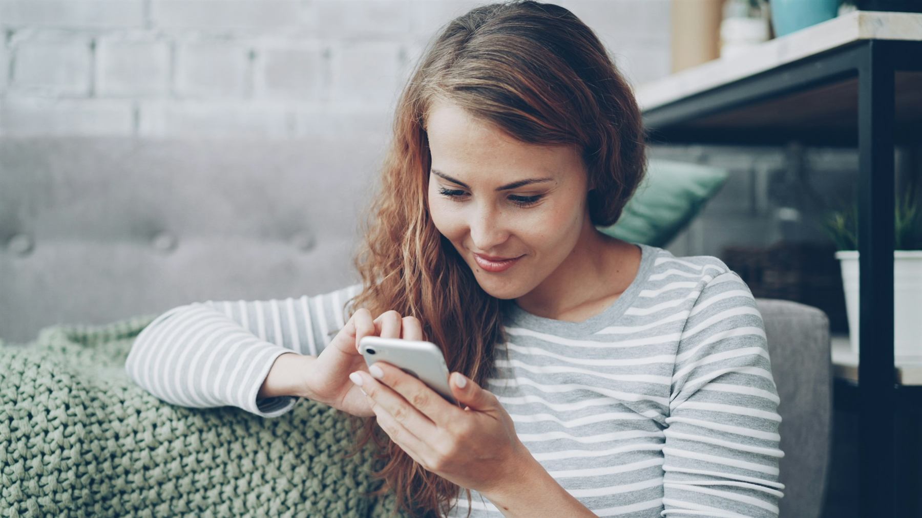A young woman smiling at her phone while relaxing on a sofa